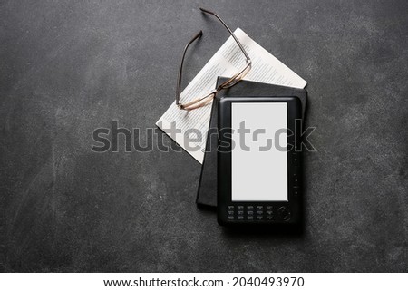 E-reader, notebook, newspaper and eyeglasses on dark background