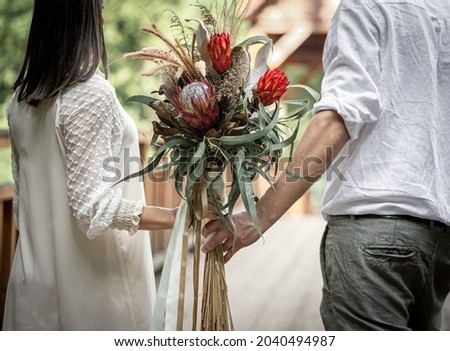 Rear view, a couple in love holding a bouquet with exotic protea flowers.