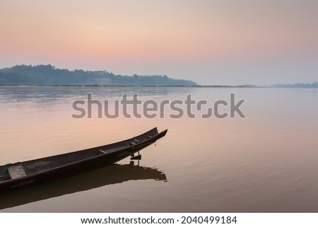 A traditional wooden boat on the Mekong Riverbank at dawn, sunrise sky reflection on surface of the river. Thailand-Laos border. Soft focus on the boat. Royalty-Free Stock Photo #2040499184