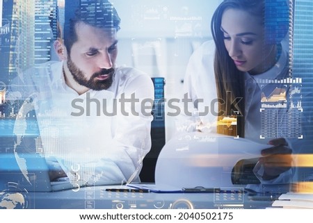 Businessman and businesswoman wearing white shirts work together typing on laptop and taking notes on clipboard. Office workplace and Singapore city skyscraper in the background. Concept of teamwork