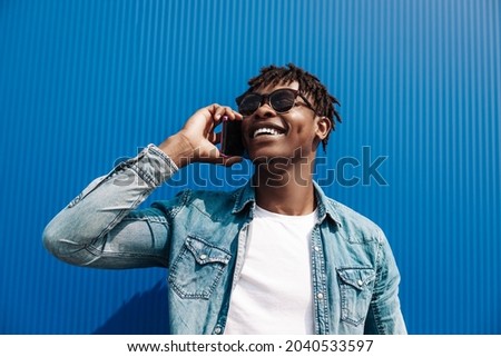 Black guy african, talking on the phone, against the background of a blue building, and the concept of success, student with a phone
