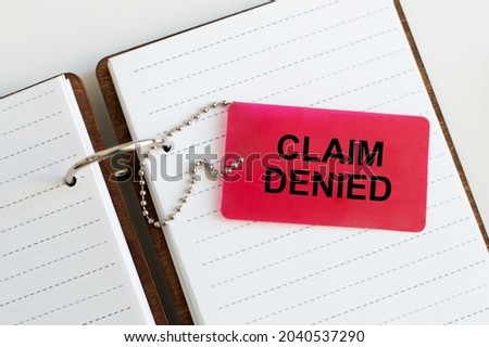 CLAIM DENIED written on a red card that lies on a white notepad on the table