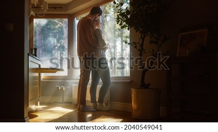 Couple At Home: Woman Watching Out of Window Male Partner Embraces Her From Behind. Happy Couple in Ideal Relationship Spending Sunny Day Together. Beautiful Family Moments Royalty-Free Stock Photo #2040549041