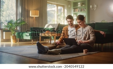 Couple Use Laptop Computer, while Sitting on the Living Floor room of their Apartment. Boyfriend and Girlfriend Talk, Shop on Internet, Choose Product to Order Online, Watch Streaming Service Royalty-Free Stock Photo #2040549122