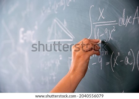 Close-up shot of a hand holding chalk and writing mathematical equations on the blackboard. Education concept.