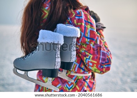 A woman in a ski suit holds skates on her shoulder, after skiing on a frozen lake, closeup