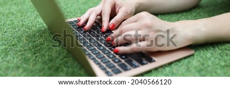 Woman lies on green lawn and works on laptop closeup
