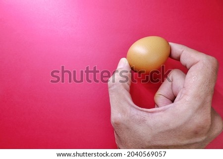 A man's hand holding one eggs, red background. high angle view, flat lay, top view, Food and drink concept. Negative space