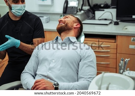 Caucasian male client chatting to nurse sitting in doctors office chair 