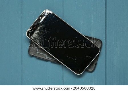 Damaged smartphone on light blue wooden table, top view. Device repairing