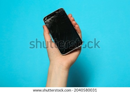 Woman holding damaged smartphone on light blue background, closeup. Device repairing