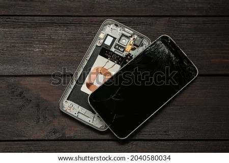 Damaged smartphone on dark wooden table, flat lay. Device repairing