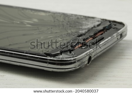 Smartphone with cracked screen on light beige wooden background, closeup. Device repair
