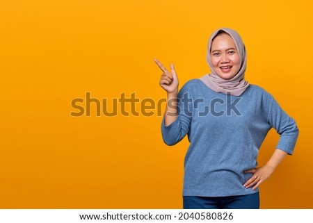 Portrait of cheerful attractive Asian woman pointing finger at empty space