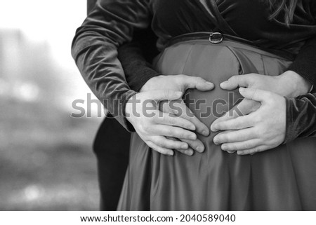 Black and white banner with the hands of a married couple in the form of a heart on the background of a pregnant belly - a symbol of love for the unborn child. Love. Future parents. Love and family