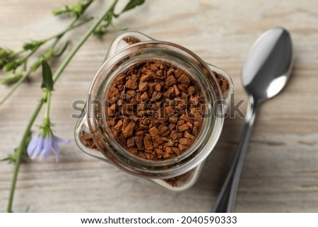 Jar of chicory granules on white wooden table, top view