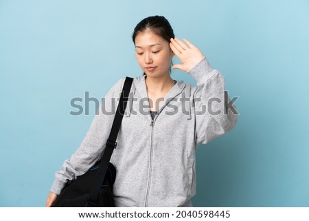 Young sport Chinese  woman with sport bag over isolated blue background making stop gesture and disappointed