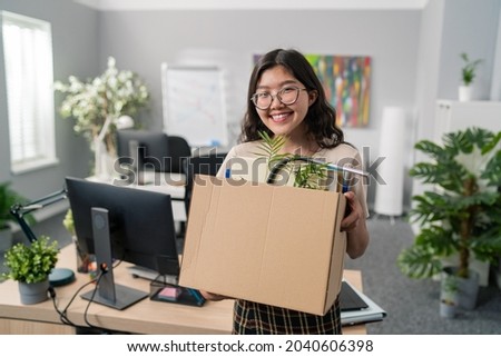 Beautiful girl with Korean Asian beauty gets a promotion in the office, changes position, carries her things packed in a box, moves them, leave job, she is happy smiling, leaves the company Royalty-Free Stock Photo #2040606398