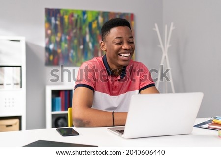 Trainee in office sits at desk in front of laptop monitor in background whiteboard, young dark skinned man talking on internet with clients, co-workers, uses webcam, video call, puzzled surprised face Royalty-Free Stock Photo #2040606440