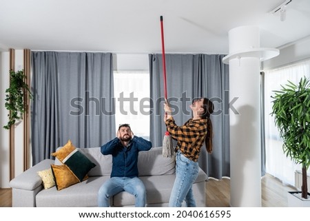 Young couple stares at the ceiling and yells because a neighbor upstairs is having a party with loud music or renovating an apartment and workers are drilling with heavy tools. Noise pollution concept Royalty-Free Stock Photo #2040616595