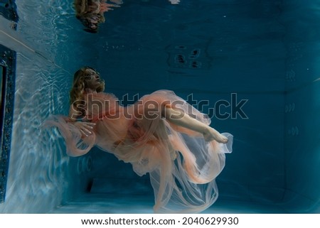 A girl with long dark hair swims underwater in a pink dress and with a crown on her head, like an underwater queen. Fairy tale suitable for advertising	