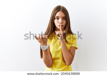 Young brunette teenager standing together over isolated background asking to be quiet with finger on lips pointing with hand to the side. silence and secret concept. 