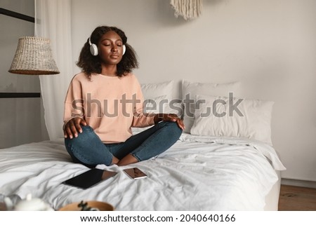 Online Meditation. Peaceful Black Woman Meditating With Eyes Closed Wearing Headphones Sitting In Lotus Position, Listening To Yoga Instructor Via Digital Tablet Relaxing In Bedroom At Home Royalty-Free Stock Photo #2040640166