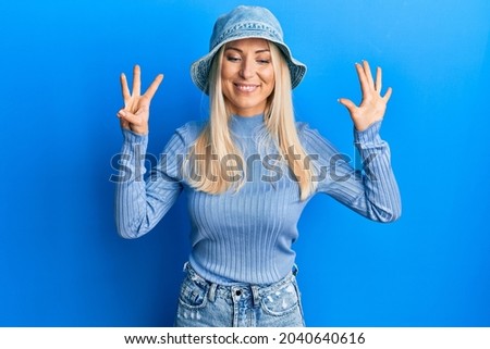 Young blonde woman wearing casual denim hat showing and pointing up with fingers number eight while smiling confident and happy. 
