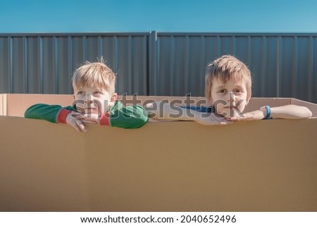 Little boys sitting inside a big carton box on the backyard