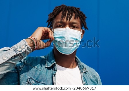 portrait of an afro american black man wearing a protective mask from the coronavirus, blue background