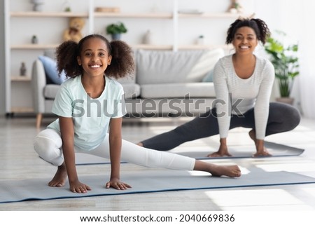 Joyful african american mother and daughter stretching legs together at home, sporty black family doing morning exercises on yoga mats in cozy living room, cheerfully smiling at camera Royalty-Free Stock Photo #2040669836