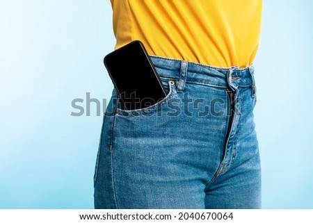 Unrecognizable woman having smartphone with empty screen in her jeans pocket on blue studio background, mockup for mobile app or website design. Space for your ad template Royalty-Free Stock Photo #2040670064