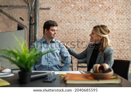 Happy down syndrome man with businesswoman colleague working in office, social inclusion and cooperation concept. Royalty-Free Stock Photo #2040685595