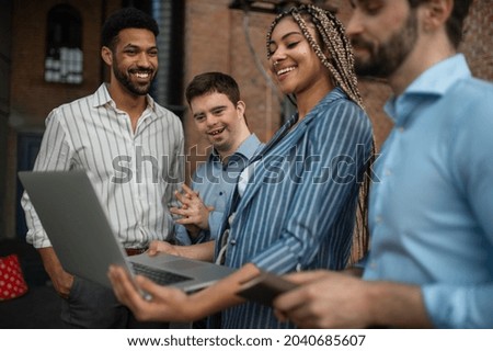 Cheerful young businesspeople with laptop working in office, social inclusion and cooperation concept. Royalty-Free Stock Photo #2040685607