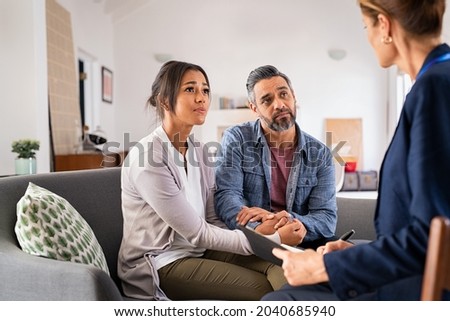 Mature stressed married couple and talking to advisor at home. Worried indian man with his african american wife discussing to healthcare agent. Multiethnic couple in conversation with social worker. Royalty-Free Stock Photo #2040685940