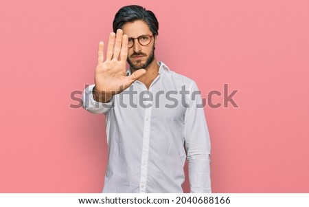 Young hispanic man wearing business shirt and glasses doing stop sing with palm of the hand. warning expression with negative and serious gesture on the face. 