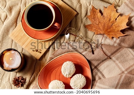 people, season and leisure concept - cup of coffee, autumn leaves, meringues and candle on warm blankets at home