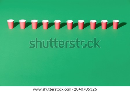 Row of red paper cup on green background with copy space. creative concept, minimalist, modern art