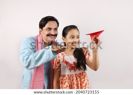 Happy Indian family of Father and daughter portraying a rural India concept. Daughter holding paper airplane in hand and both are dreaming for flying abroad and accomplishing the goals of life. Royalty-Free Stock Photo #2040723155