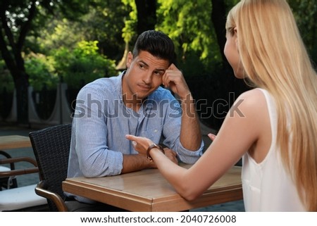 Man having boring date with talkative woman in outdoor cafe