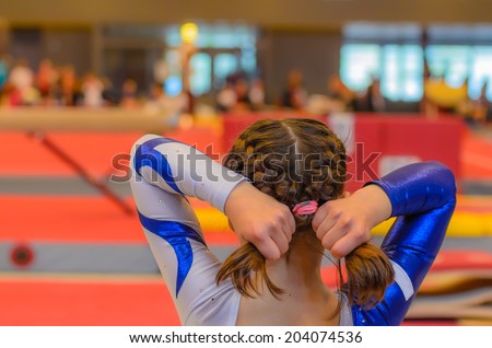 Young gymnast girl fixing her hair with ponytail before appearance on the local competition Royalty-Free Stock Photo #204074536