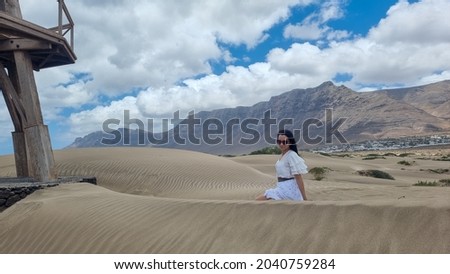 A vertical shot of a Caucasian woman in a beautiful white dress sitting o a sand in Spain