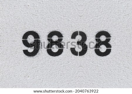 Black Number 9838 on the white wall. Spray paint. Number nine thousand eight hundred thirty eight.
