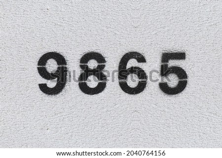 Black Number 9865 on the white wall. Spray paint. Number nine thousand eight hundred and sixty five.