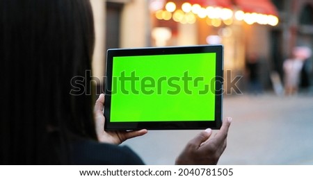 Female hands holding tablet with green screen. Girl using mobile phone while walking in the autumn street. Back view shot. Chroma key, close up woman hand holding device with vertical green screen 