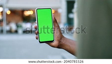 Male hands holding smartphone with green screen. Guy using mobile phone while walking in the autumn street. Back view shot. Chroma key, close up man hand holding phone with vertical green screen 