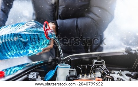 The male driver pours antifreeze into the tank to spray the windshield during a snowstorm. Royalty-Free Stock Photo #2040799652