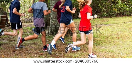 High school cross country runners training in a park on the grass passing a bench and a tree together. Royalty-Free Stock Photo #2040803768