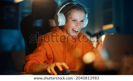 Excited Young Boy in Headphones Playing Video Games on Laptop Computer in Cozy Dark Room at Home. Happy Successful Teenager Beating Players and Winning at the Online Competition.