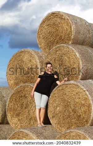 Girl posing near a stack of straw. Straw rolls, stacked in a pyramid.